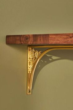 a wooden shelf with a gold decoration on the top and bottom, against a green wall