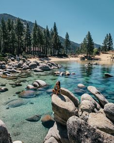 a woman sitting on rocks in the middle of a body of water with clear blue water