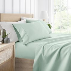 a bed with light green sheets and pillows