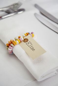 a white table topped with a napkin covered in colorful beaded bracelets next to silverware