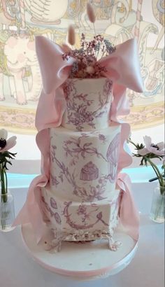 a three tiered cake with pink bows and flowers in vases on the table