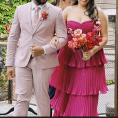 a man in a suit and tie walking with a woman in a pink dress behind him