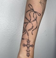 a woman's arm with a cross and rosary tattoo design on it, in black ink