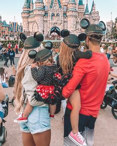 three people with mickey ears on their heads in front of a castle at disney world