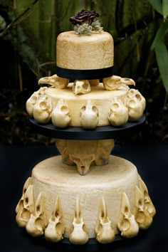 three tiered cake with skulls and flowers on the top, sitting in front of plants