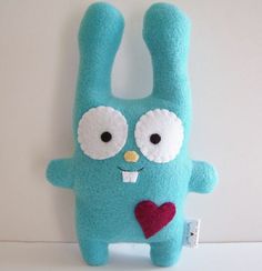 a blue stuffed animal with big eyes and a heart in its mouth, hanging on a white wall