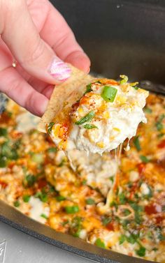 a hand holding a tortilla chip and scooping it into a skillet