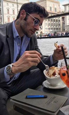 a man sitting at a table eating food with a drink in front of him and looking down