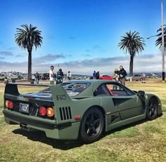 a green sports car parked on top of a grass covered field next to palm trees