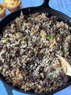 a skillet filled with rice and meat on top of a table next to muffins