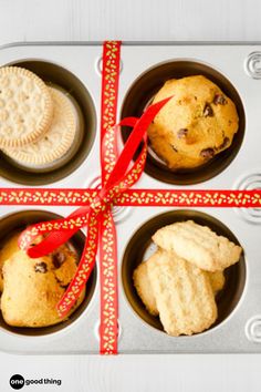 four cupcakes in a muffin tin with a red ribbon