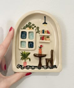 a hand holding a ceramic plate with miniature furniture on it