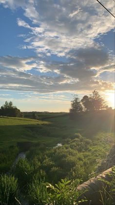 the sun shines brightly over an open field and stream in the foreground, with trees on either side