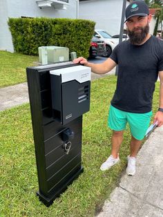 a man standing next to an electronic device on the side of a road in front of a house