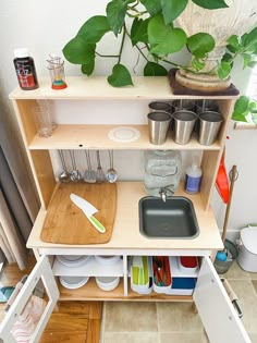 a wooden shelf filled with pots and pans on top of a tiled floor next to a potted plant