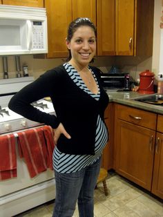 a pregnant woman standing in a kitchen with her hands on her hips and smiling at the camera