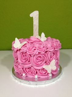 a pink birthday cake with white butterflies on top and the number one frosted in icing