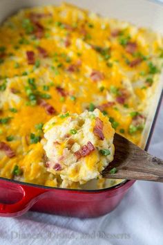 a red casserole dish filled with potatoes and bacon, garnished with green onions