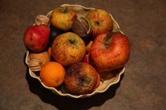 a bowl filled with lots of fruit on top of a brown countertop next to oranges and apples