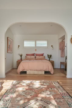 a large bed sitting under a window next to a wooden floor covered in pink pillows