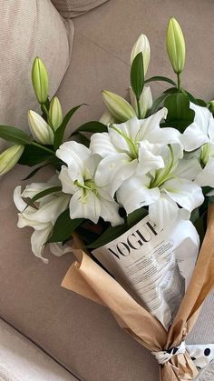 a bouquet of white flowers sitting on top of a couch next to a newspaper bag