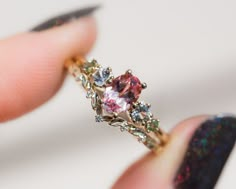 a woman's hand holding a ring with an orange and pink stone