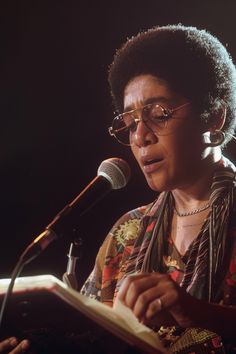 a woman reading a book in front of a microphone