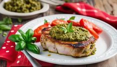 a white plate topped with meat covered in pesto sauce and tomatoes on top of it