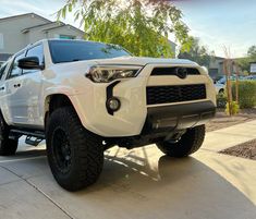 a white toyota truck parked in front of a house next to a tree and bushes