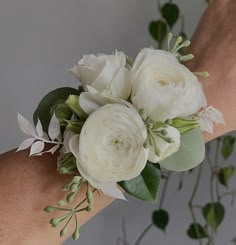 a bouquet of white flowers is being held by someone's arm with greenery