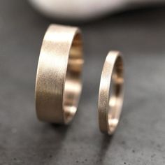 two gold wedding rings sitting on top of a gray table next to a white object