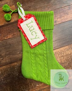 a green christmas stocking with a tag hanging from it's side on a wooden floor