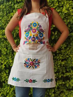 a woman standing in front of a green hedge wearing an apron with flowers on it