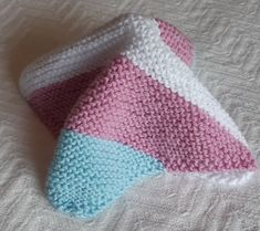 a crocheted pink, white and blue hat laying on top of a bed