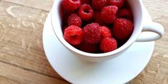 raspberries in a white cup on a wooden table