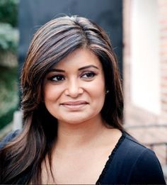 a woman with long brown hair and black shirt smiling at the camera while standing in front of a brick building