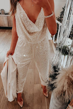 a woman taking a selfie while wearing a white sequin jumpsuit and heels