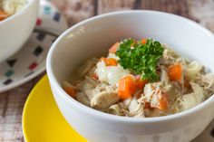 a white bowl filled with chicken and carrots next to a yellow plate on a table