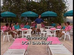 a man standing in front of a group of people sitting at tables with umbrellas