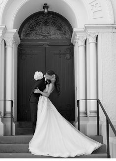 a bride and groom kissing in front of the doors of an old church on their wedding day