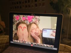 a laptop computer sitting on top of a bed with two women's faces painted red