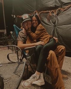 two people sitting on a bench in front of a tarp covered tent with their arms around each other