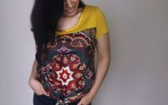 a woman with long black hair wearing a yellow shirt and blue jeans is standing in front of a white wall