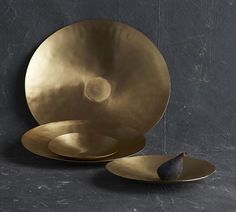 two brass plates sitting on top of a black table next to each other with an olive in the middle