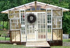 a small house made out of old windows and doors with a wreath on the front door