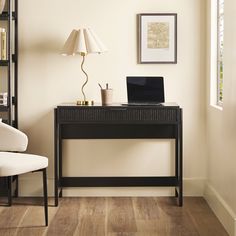 a laptop computer sitting on top of a wooden desk next to a lamp and chair