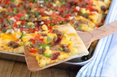 a pizza with sausage, peppers, and cheese on a wooden spatula next to a baking pan