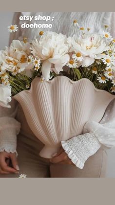 a woman holding a vase filled with white flowers