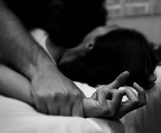 two hands touching each other while laying on top of a white bed in black and white