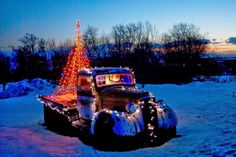 an old car is decorated with christmas lights and a lighted tree in the back ground